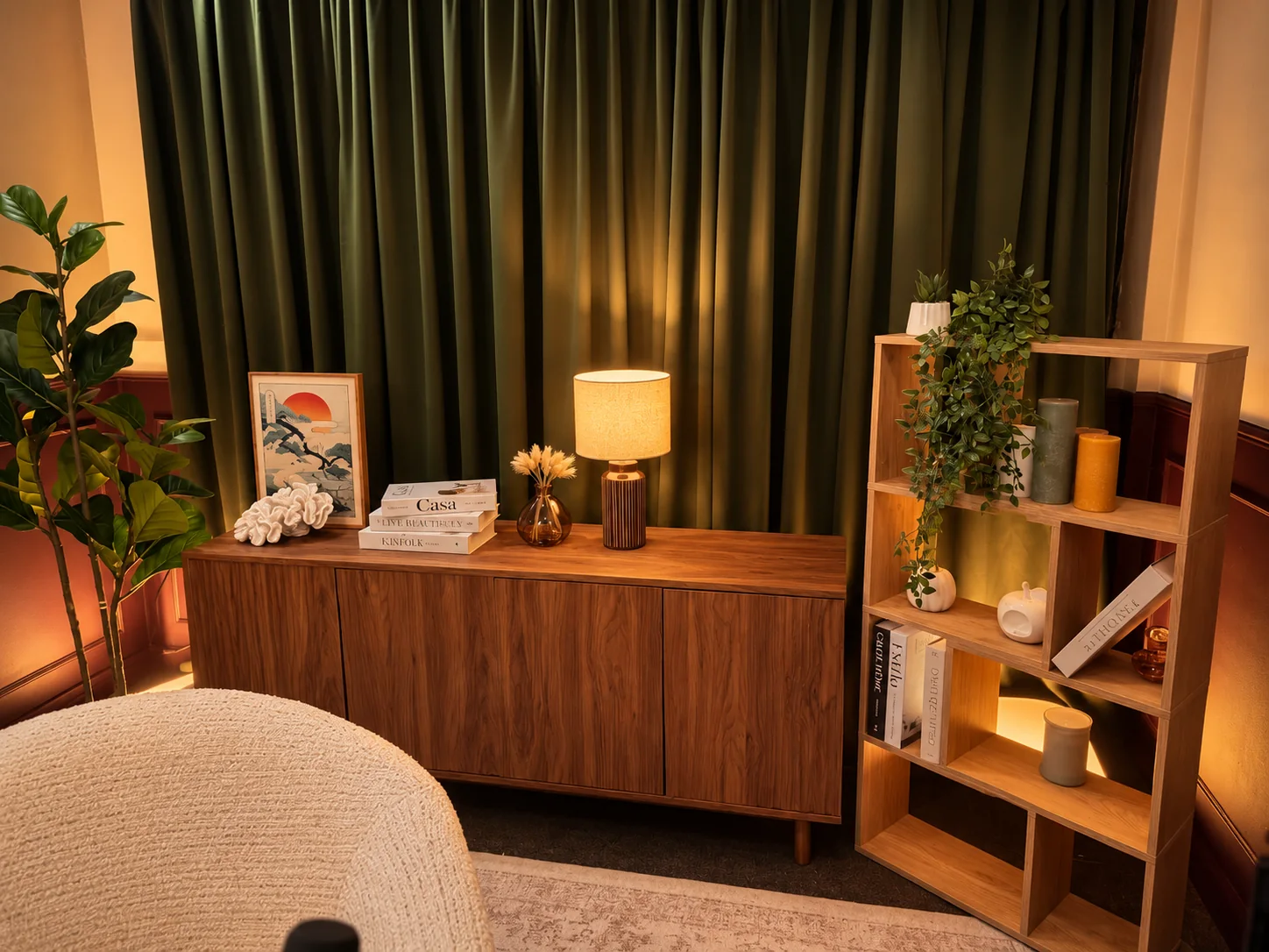 Olive curtains, a glowing table lamp and plants surrounding the studio armchair